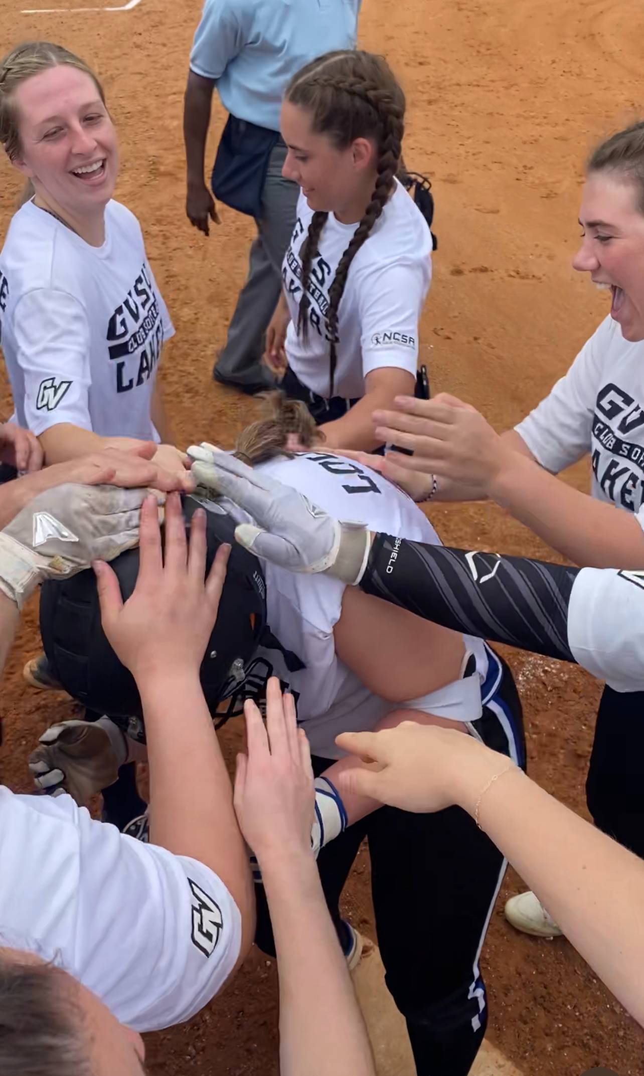 softball player crossing home plate with teammates cheering around her and all hands on her helmet